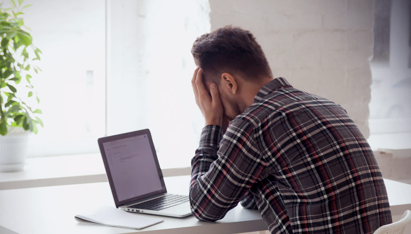 man holding his head in hands in front of a ransomware infected laptop