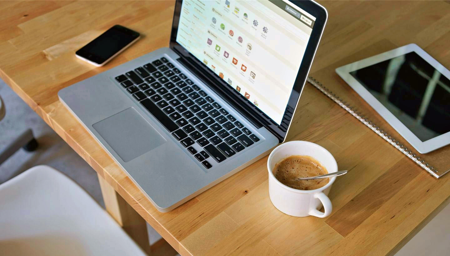 laptop on a desk with a cup of coffee, cell phone, and iPad