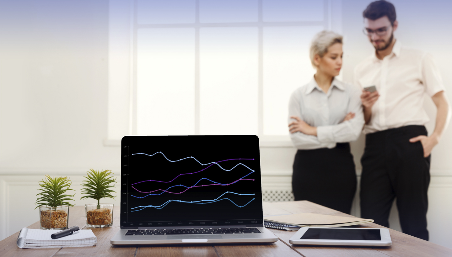 computer with line chart on a desk with a man and woman standing near it