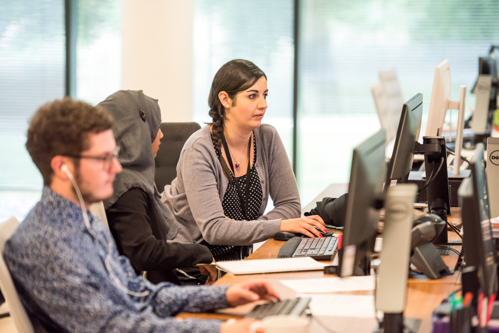 a row of office computers with two women and a man working 