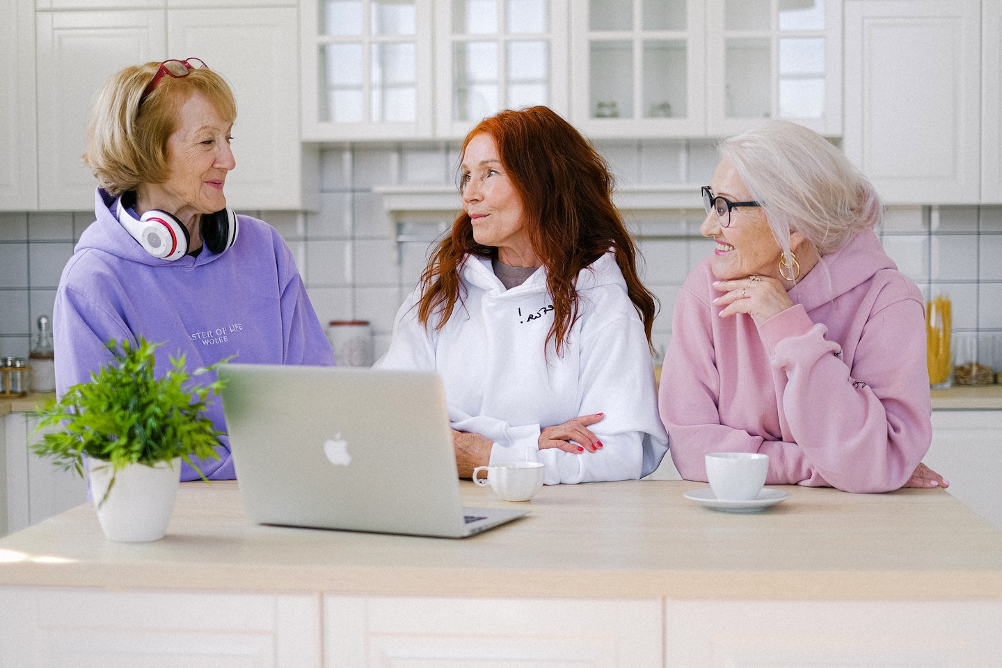 A image of three women sitting at a counter drinking coffee in front of an open laptop.