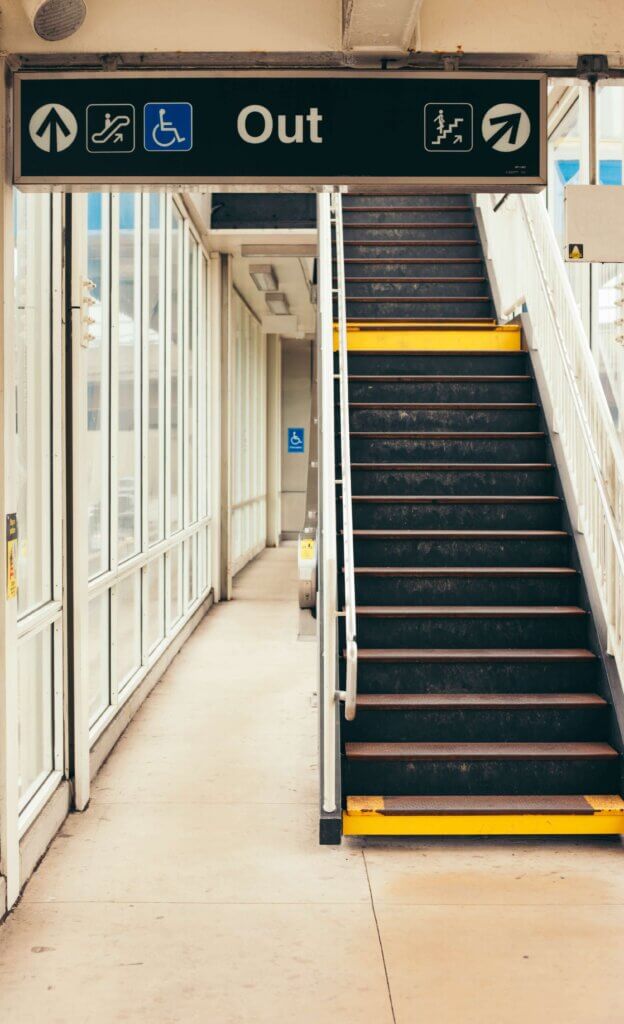 A photo of a stair case with a sign that says "out" and an arrow pointing up. 